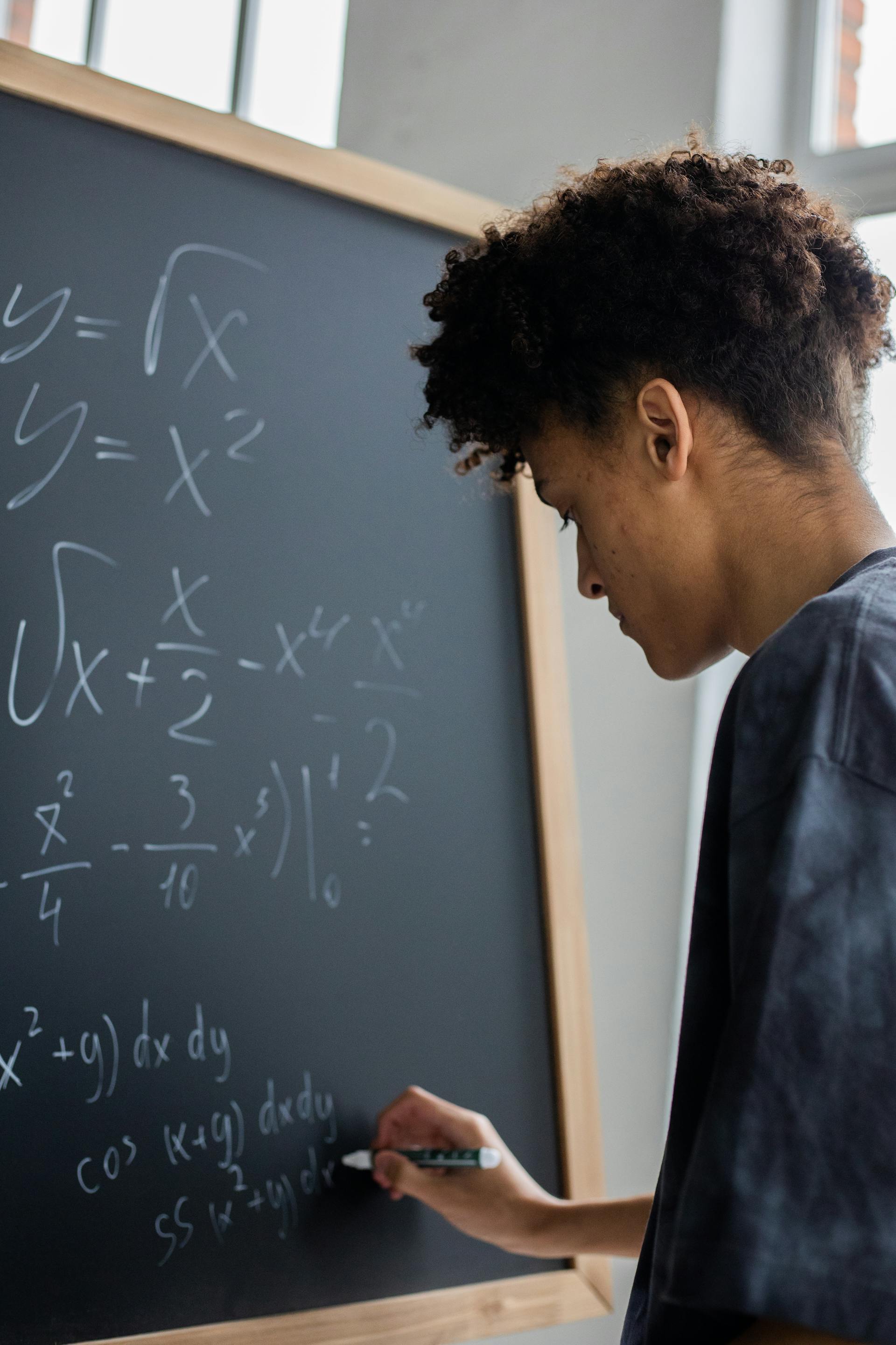 Persona escribiendo ecuaciones matemáticas en una pizarra, incluyendo integrales y expresiones algebraicas.
